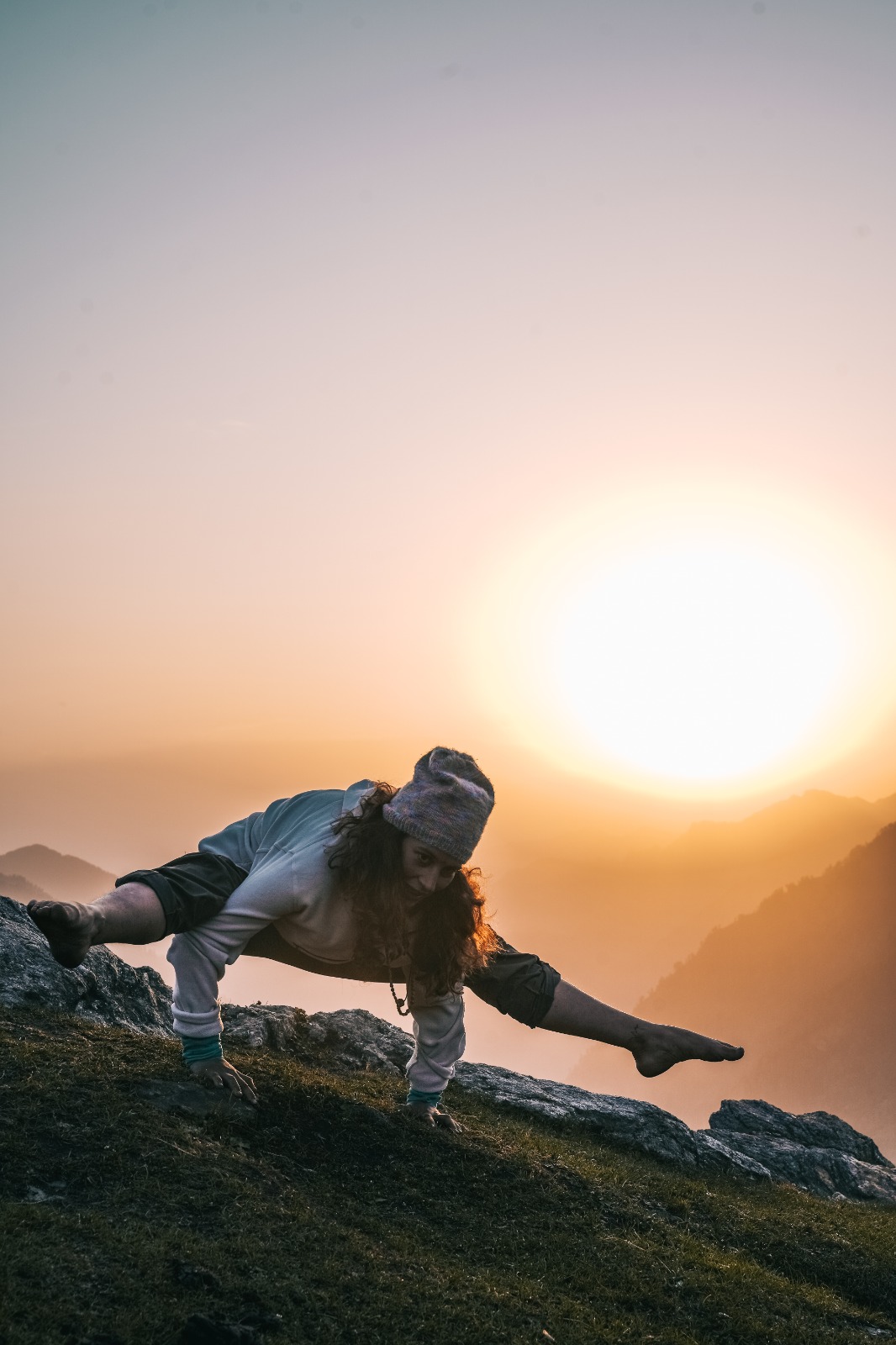 Woman holding an arm-balance yoga pose on a mountain ridge at sunrise